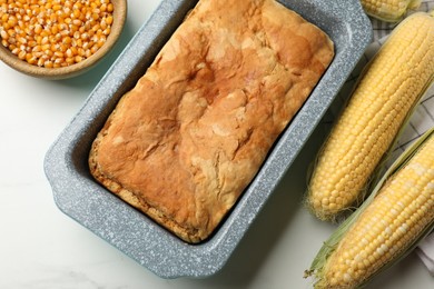 Photo of Freshly baked cornbread, seeds and cobs on white marble table, flat lay