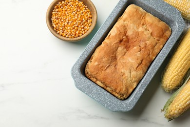 Photo of Freshly baked cornbread, seeds and cobs on white marble table, flat lay. Space for text