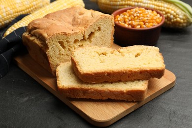 Photo of Freshly baked cornbread, cobs and seeds on black table, closeup