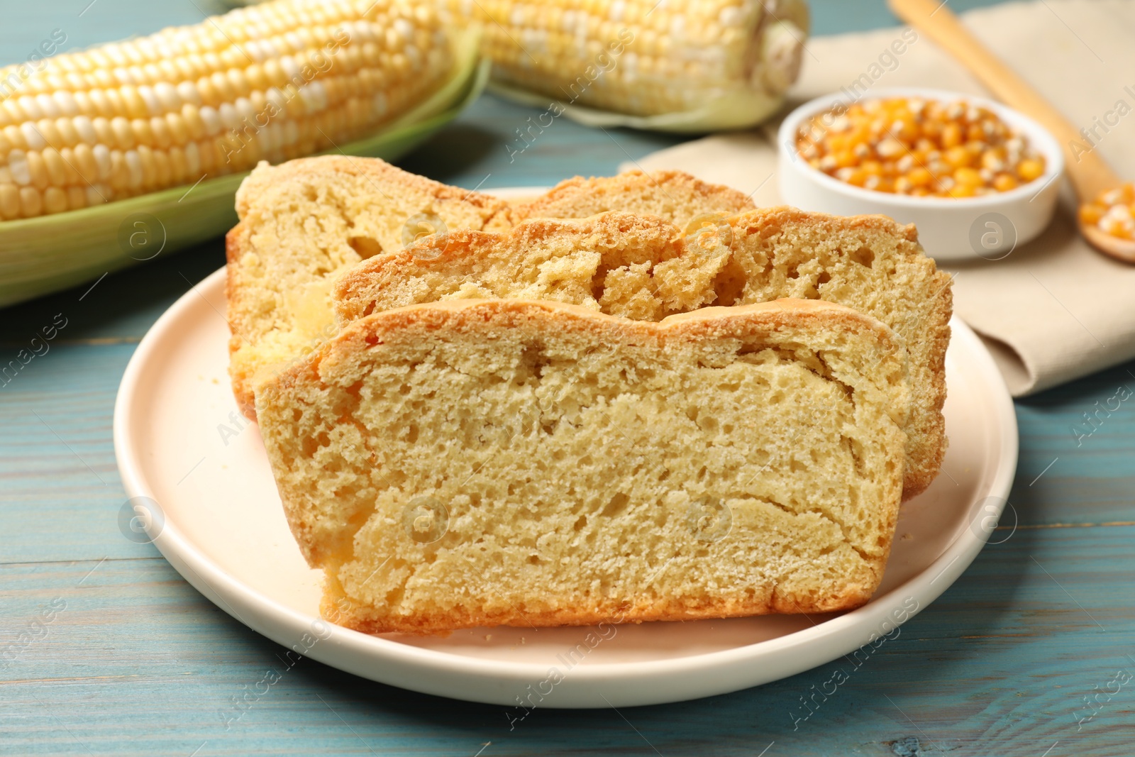 Photo of Freshly baked cornbread, cobs and seeds on light blue wooden table, closeup