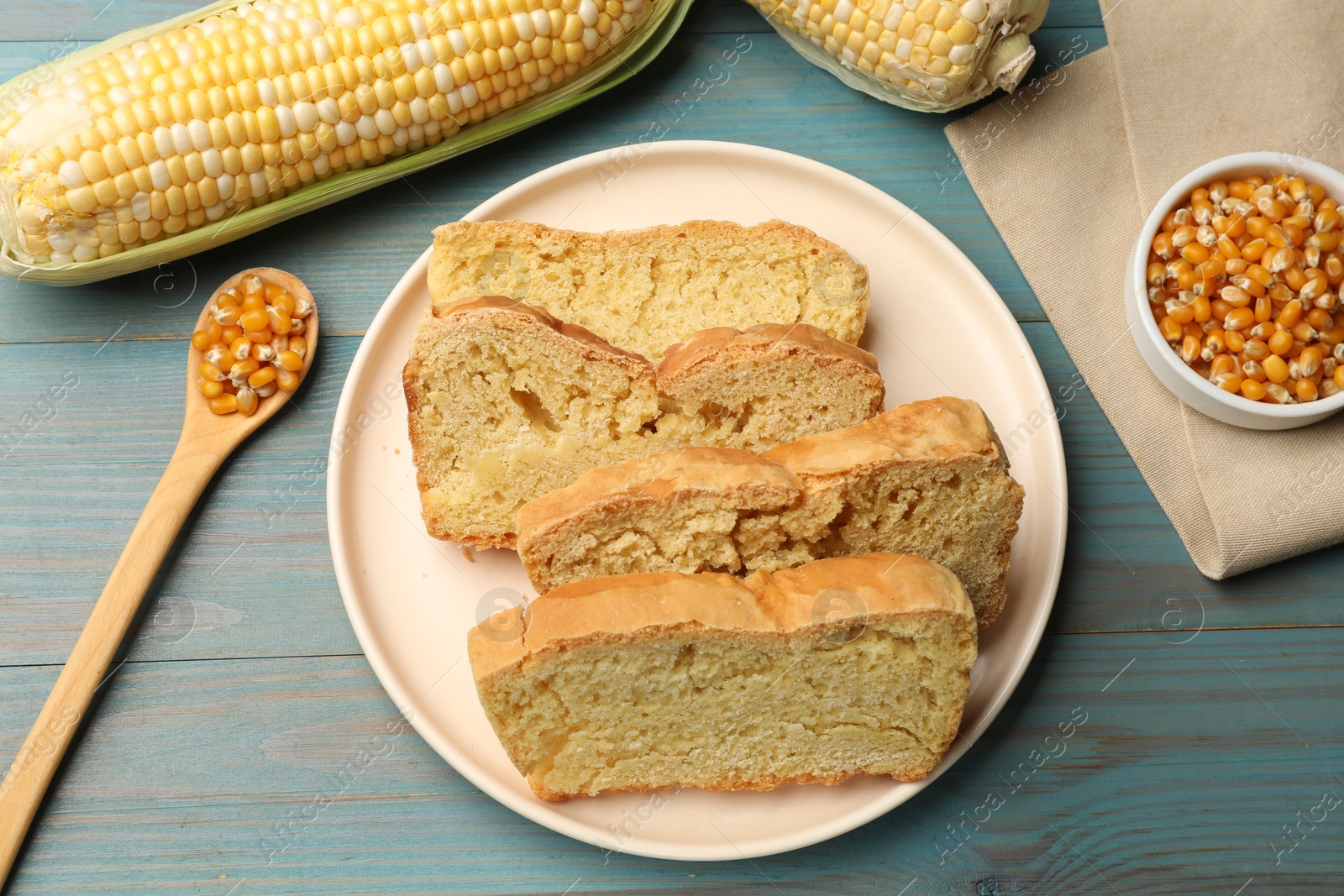 Photo of Freshly baked cornbread, cobs and seeds on light blue wooden table, flat lay
