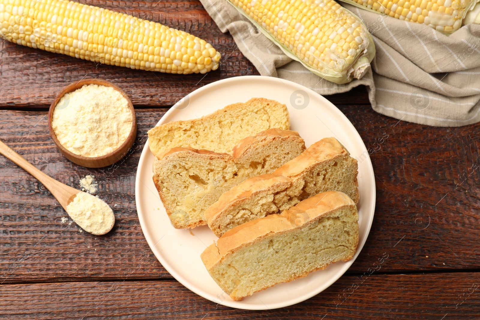 Photo of Freshly baked cornbread, cobs and flour on wooden table, flat lay
