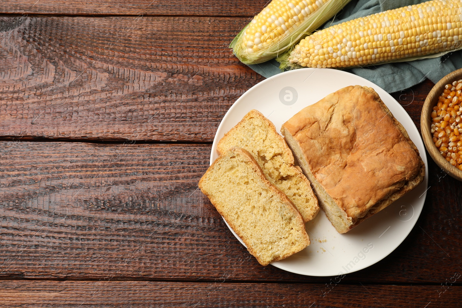 Photo of Freshly baked cornbread, cobs and seeds on wooden table, flat lay. Space for text