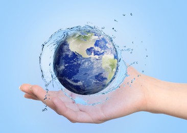 Image of Save water concept. Earth surrounded by splashing water in woman's hand against pale blue background