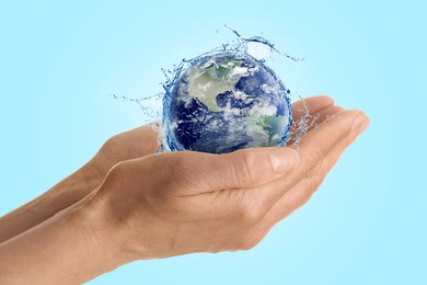 Image of Save water concept. Earth surrounded by splashing water in woman's hands against light blue background