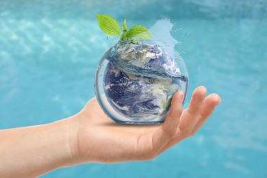 Image of Save water concept. Earth and plant branch inside aquarium bowl with splashing water in human hand against sea surface