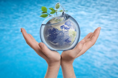 Image of Save water concept. Earth and plant branches inside aquarium bowl with splashing water in man's hands against sea surface