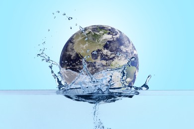 Image of Save water concept. Earth falling into water against light blue background