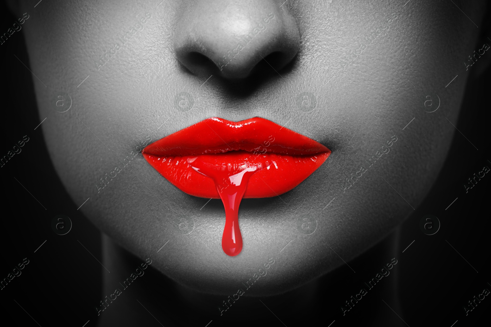 Image of Red liquid lipstick dripping from woman's lip, closeup. Black and white toning with color accent
