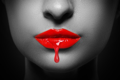 Image of Red liquid lipstick dripping from woman's lip, closeup. Black and white toning with color accent
