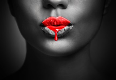 Image of Red liquid lipstick dripping from woman's lip, closeup. Black and white toning with color accent