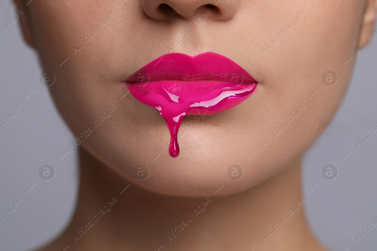 Image of Pink liquid lipstick dripping from woman's lip against grey background, closeup