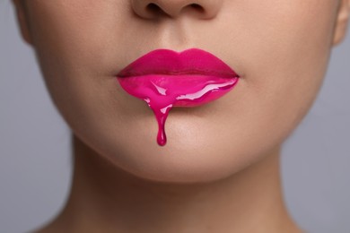 Image of Pink liquid lipstick dripping from woman's lip against grey background, closeup