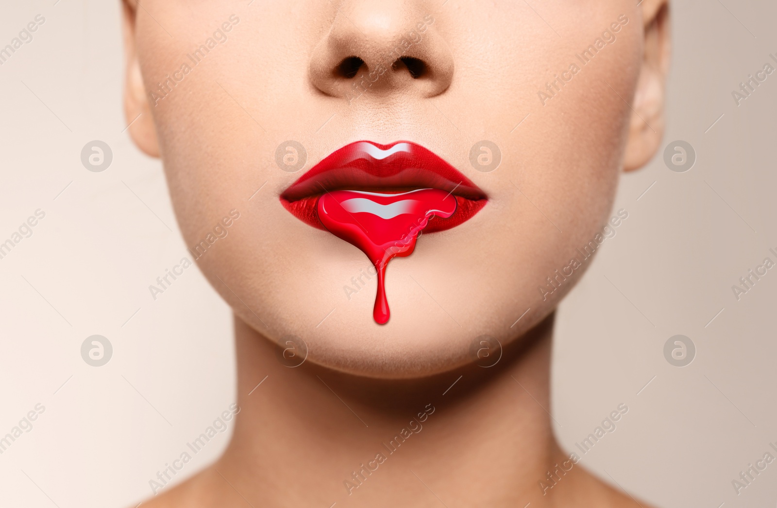 Image of Red liquid lipstick dripping from woman's lip against beige grey background, closeup