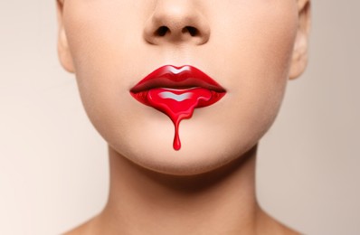 Image of Red liquid lipstick dripping from woman's lip against beige grey background, closeup