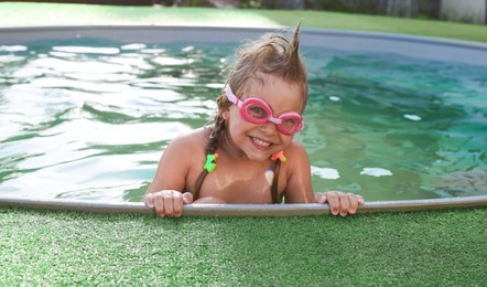 Photo of Cute little girl wearing googles in swimming pool at resort