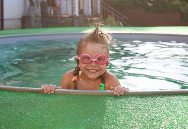 Photo of Cute little girl wearing googles in swimming pool at resort