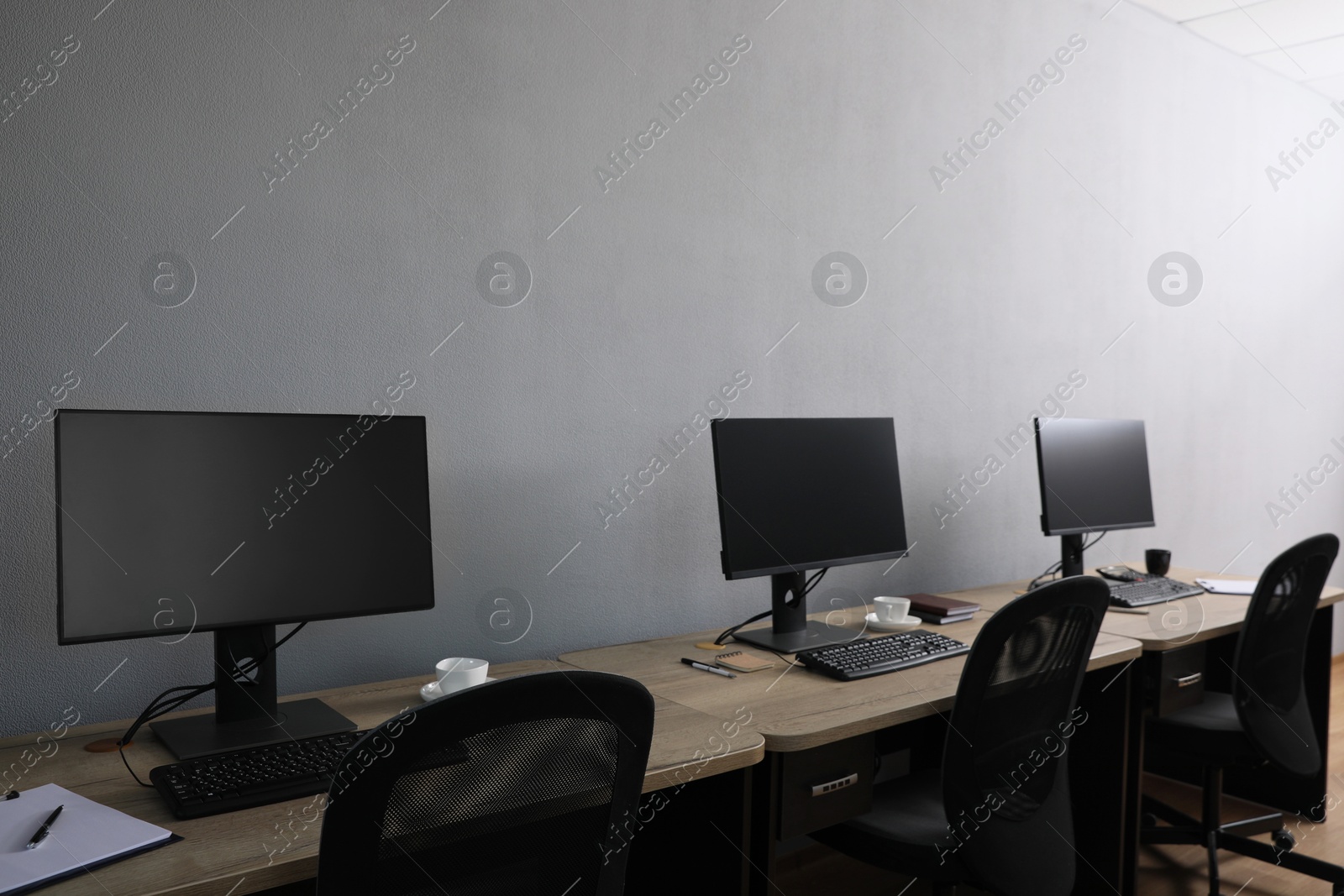 Photo of Open office interior. Modern workplaces with computers near light grey wall