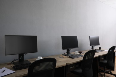 Photo of Open office interior. Modern workplaces with computers near light grey wall