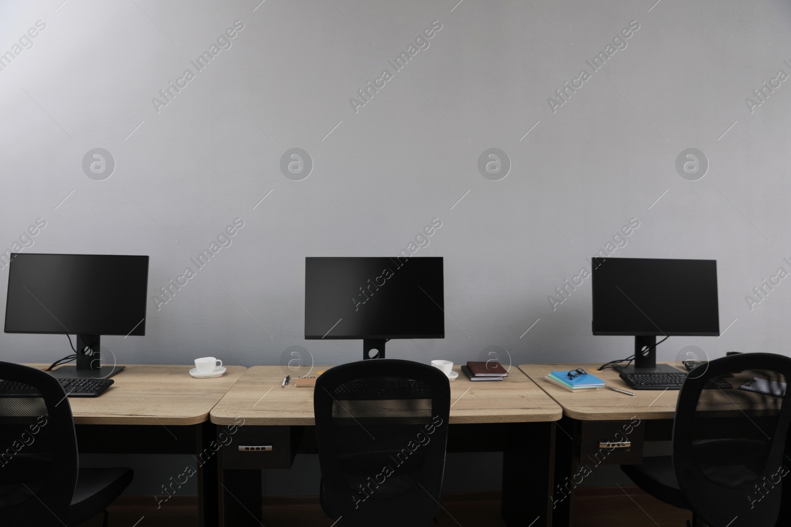 Photo of Open office interior. Modern workplaces with computers near light grey wall
