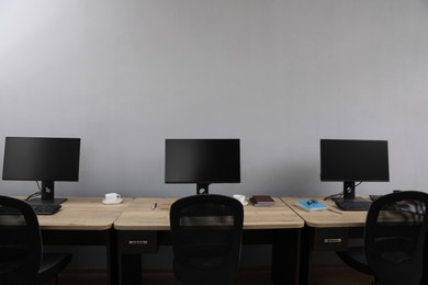 Photo of Open office interior. Modern workplaces with computers near light grey wall