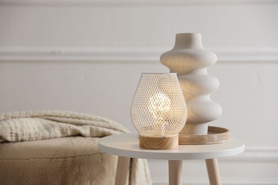 Photo of Stylish lamp and vase on white table near pouf indoors