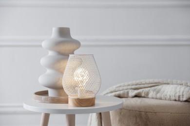 Photo of Stylish lamp and vase on white table near pouf indoors