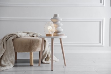 Photo of Stylish lamp and vase on white table near pouf indoors, space for text