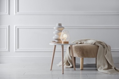 Photo of Stylish lamp and vase on white table near pouf indoors, space for text