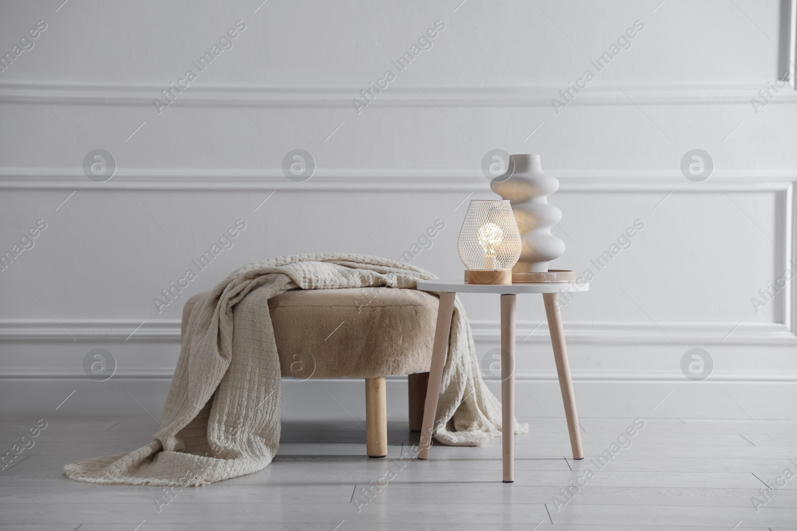 Photo of Stylish lamp and vase on white table near pouf indoors
