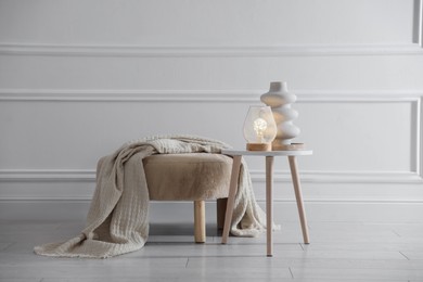 Photo of Stylish lamp and vase on white table near pouf indoors