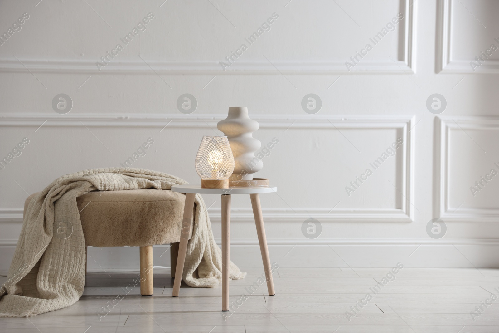Photo of Stylish lamp and vase on white table near pouf indoors, space for text