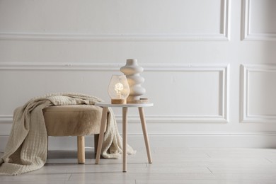 Photo of Stylish lamp and vase on white table near pouf indoors, space for text