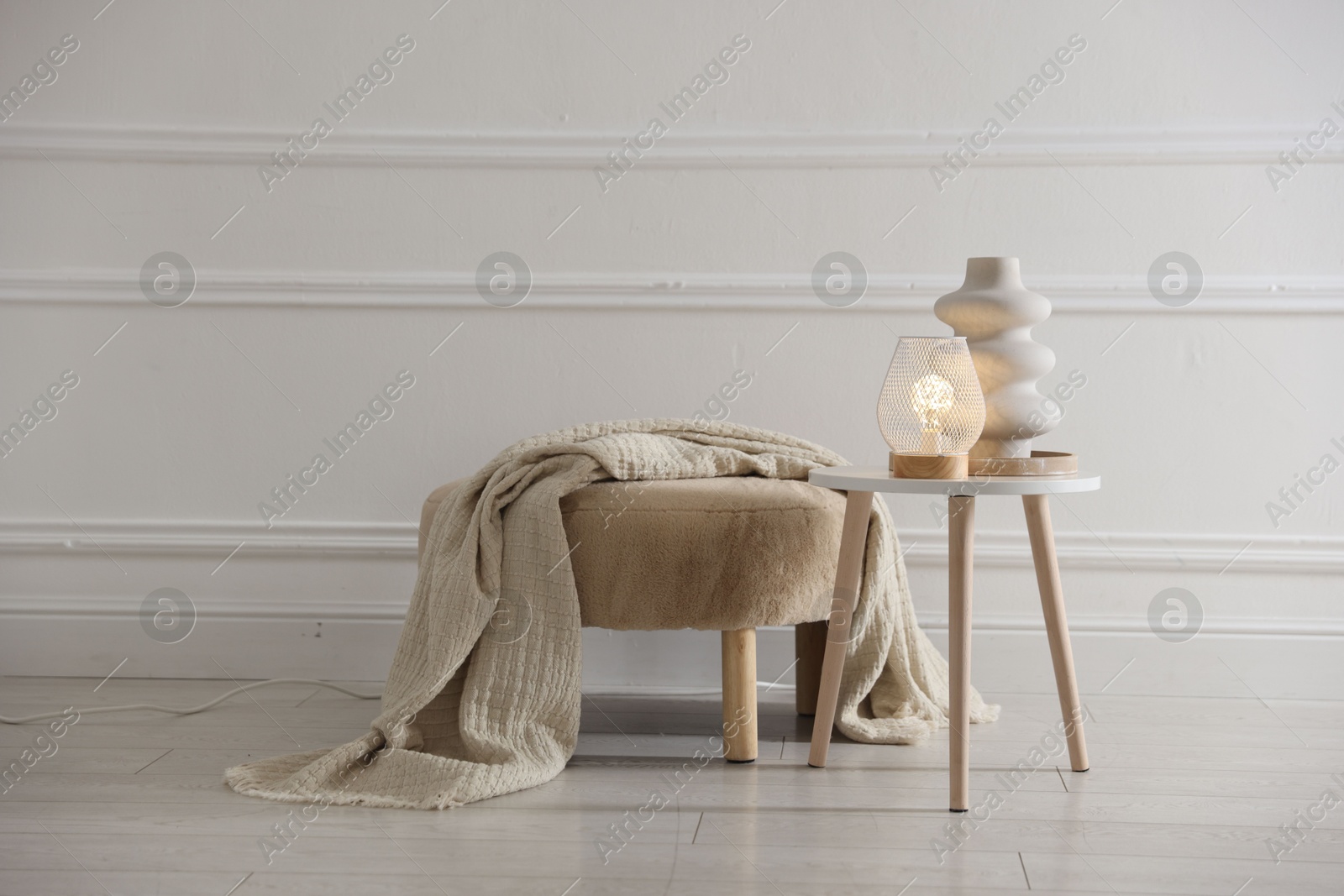 Photo of Stylish lamp and vase on white table near pouf indoors