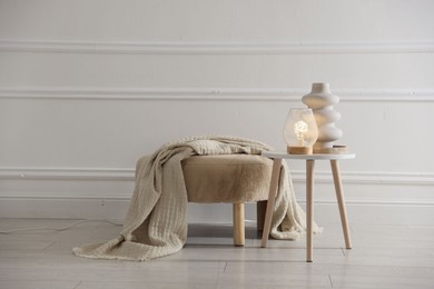 Photo of Stylish lamp and vase on white table near pouf indoors