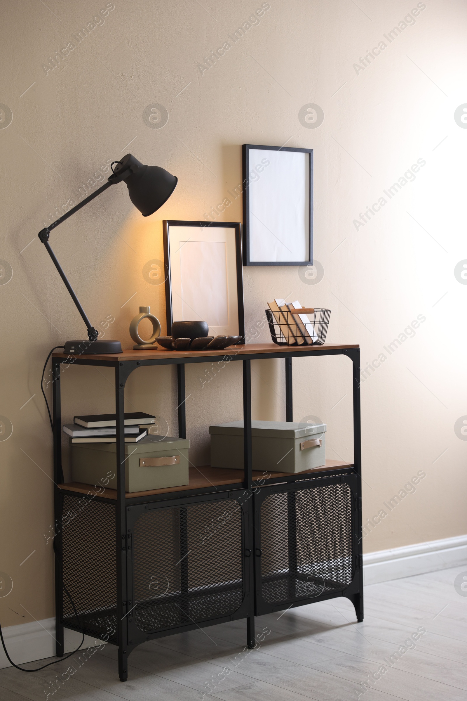 Photo of Stylish lamp, other decor and books on console table near beige wall indoors