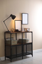 Photo of Stylish lamp, other decor and books on console table near beige wall indoors