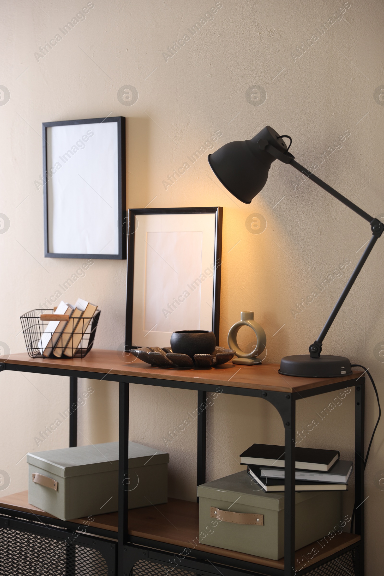 Photo of Stylish lamp, other decor and books on console table near beige wall indoors