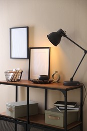 Photo of Stylish lamp, other decor and books on console table near beige wall indoors