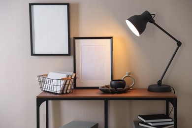 Photo of Stylish lamp, other decor and books on console table near beige wall indoors