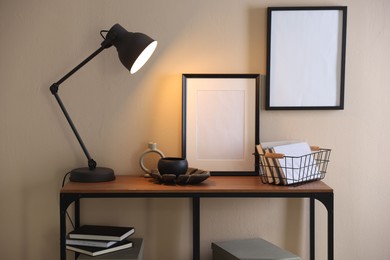 Photo of Stylish lamp, other decor and books on console table near beige wall indoors