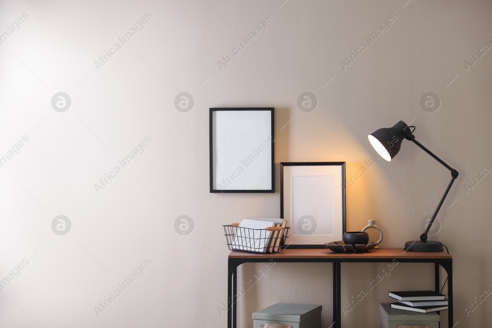 Photo of Stylish lamp, other decor and books on console table near beige wall indoors, space for text