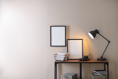 Photo of Stylish lamp, other decor and books on console table near beige wall indoors, space for text