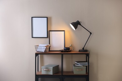 Photo of Stylish lamp, other decor and books on console table near beige wall indoors