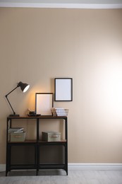Photo of Stylish lamp, other decor and books on console table near beige wall indoors, space for text