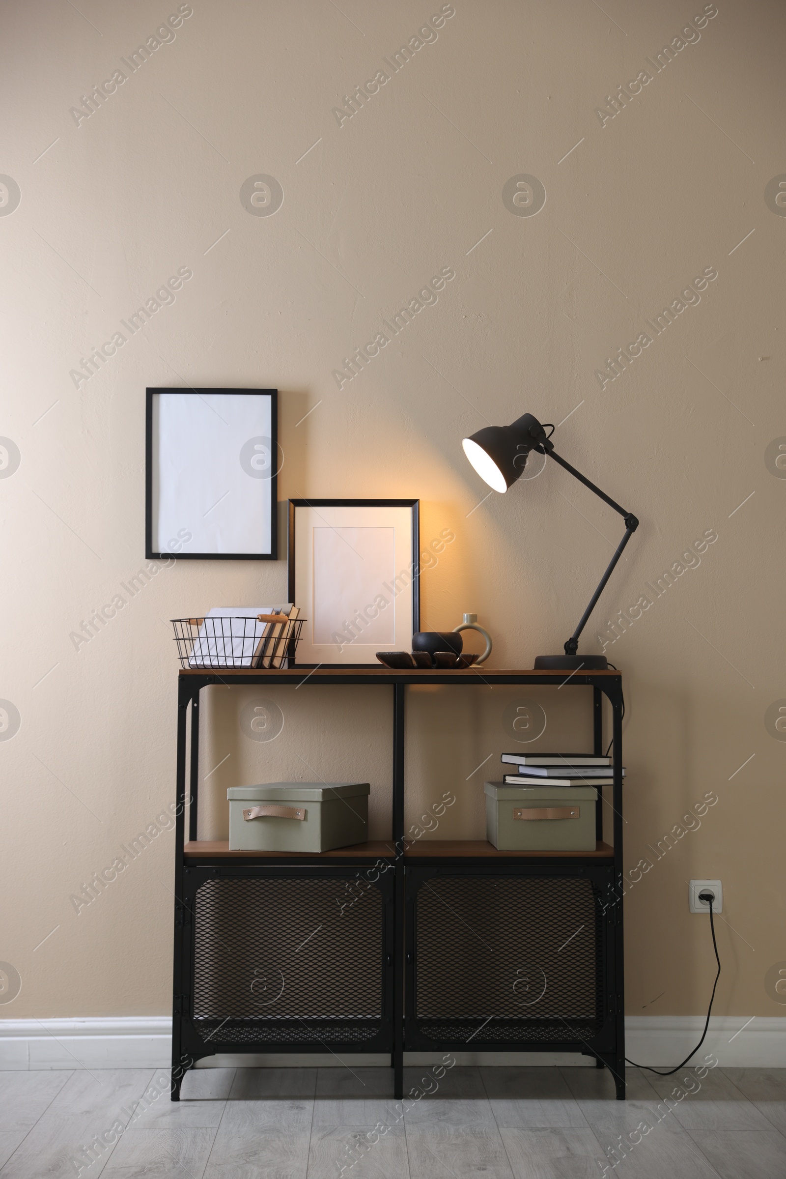 Photo of Stylish lamp, other decor and books on console table near beige wall indoors