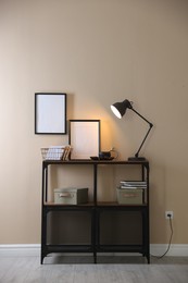 Photo of Stylish lamp, other decor and books on console table near beige wall indoors