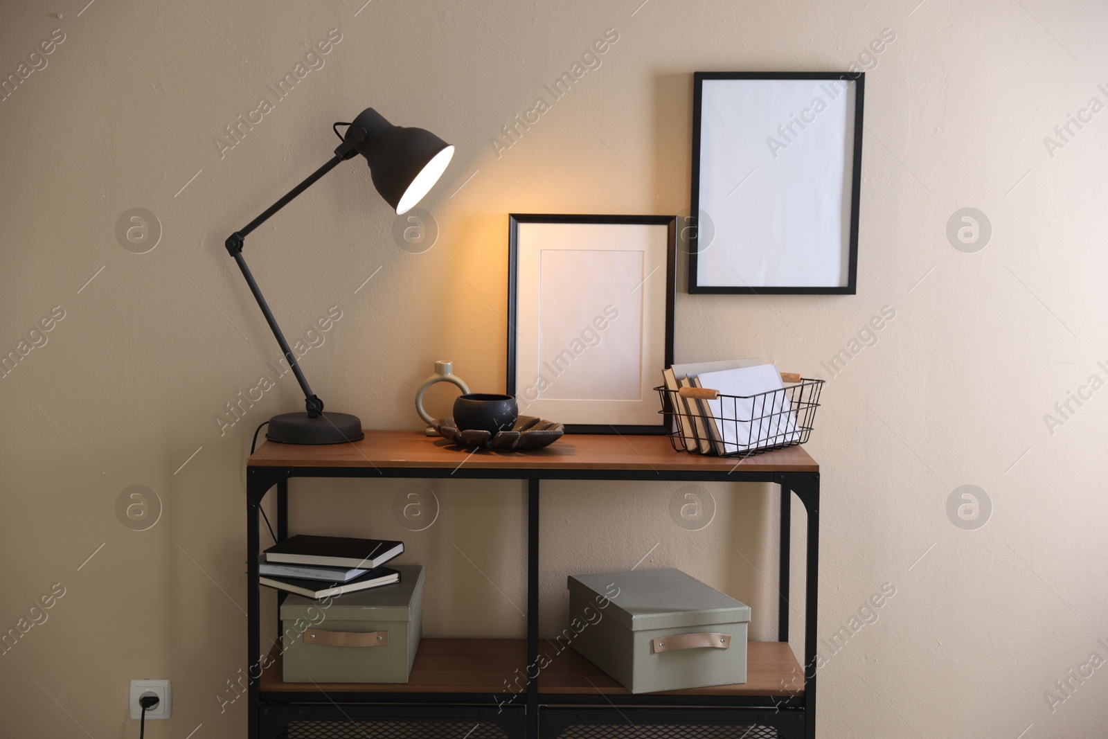 Photo of Stylish lamp, other decor and books on console table near beige wall indoors