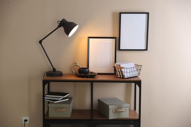 Photo of Stylish lamp, other decor and books on console table near beige wall indoors