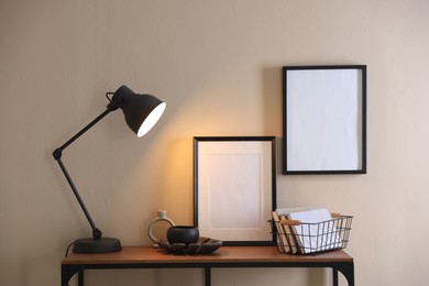 Photo of Stylish lamp, other decor and books on console table near beige wall indoors